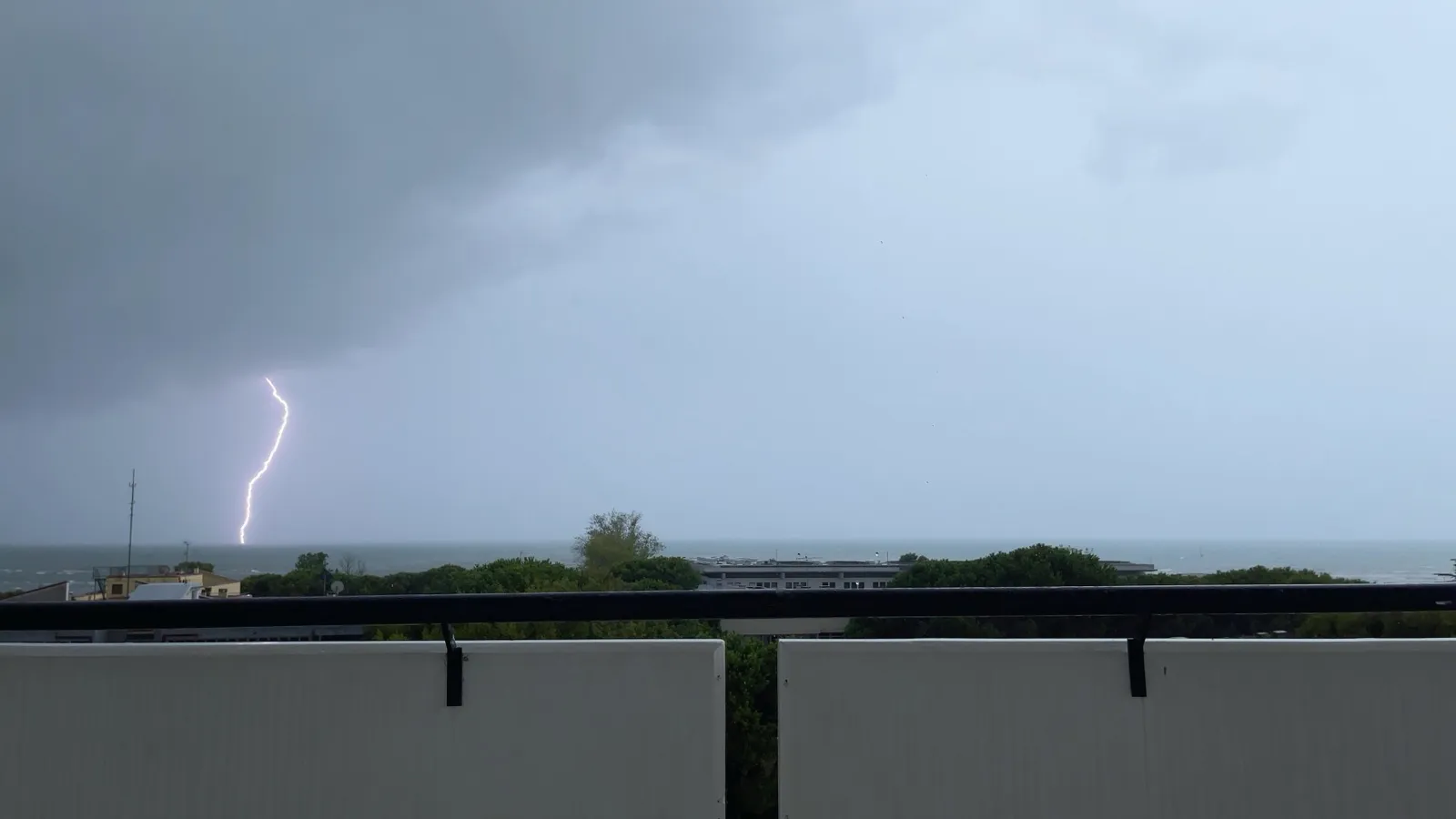 A single lightning bolt hitting the sea under a grey sky, seen from a balcony.